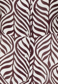 Tissu blanc avec un motif abstrait de feuilles marron foncé et une rangée verticale de petits boutons blancs.