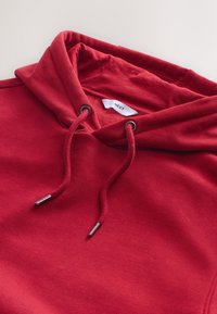 Rode capuchontrui gemaakt van zachte stof, met een trekkoord met metalen uiteinden en een label aan de binnenkant van de kraag.