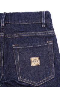 Farkkuhousut tummansinisestä kankaaasta, joissa on takatasku, jossa on neliömäinen nahkalaatta, johon on painettu "B/R" ja vaaleampi ommel.