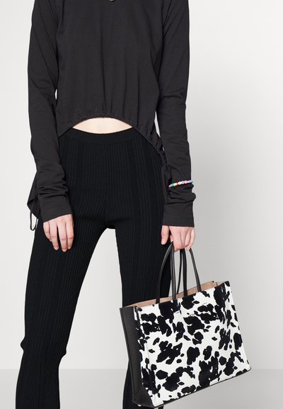 Top preto cropped de manga longa, calças altas com faixa canelada pretas e uma bolsa tote em padrão de vaca preto e branco com alças pretas.