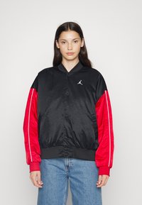 Černá a červená bomber bunda s hladkým materiálem, žebrovanými manžetami a logem na hrudi. Obsahuje knoflíkové zapínání a boční kapsy.