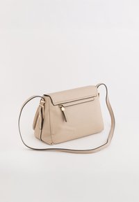 Beżowa torebka w strukturalnym kształcie z chropowatą fakturą, złotymi akcentami i odpinanym paskiem. Posiada zamek błyskawiczny i przednią kieszeń.