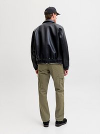 Black faux leather jacket with a ribbed hem, paired with olive cargo pants, black shoes, and a black cap. Visible stitching detail on jacket.