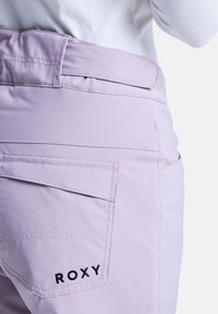 Helle lavendelfarbene Hose mit einem geschwungenen Bund, Gesäßtaschen und schwarzem "ROXY" Logo-Stickerei. Glattes Material mit taillierter Passform.
