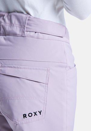 Light lavender pants featuring a curved waistband, back pockets, and black "ROXY" logo embroidery. Smooth fabric with a tailored fit.