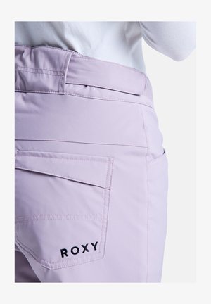 Light lavender pants featuring a curved waistband, back pockets, and black "ROXY" logo embroidery. Smooth fabric with a tailored fit.