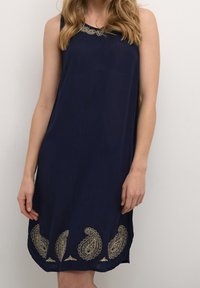 Marineblaue ärmellose Kleid mit einem Spitzen-Ausschnitt, verziert mit aufwendiger goldener Paisley-Stickerei am Saum. Leichtes Material, lockere Passform.