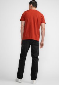 Camiseta de algodón roja con mangas cortas, cuello redondo y un corte relajado, combinada con jeans de mezclilla negros y zapatillas blancas.