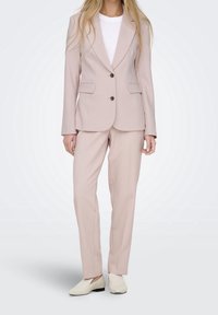 Costume rose pâle avec un blazer ajusté à deux boutons et poches, accompagné d'un pantalon assorti. Tissu lisse et design minimaliste.