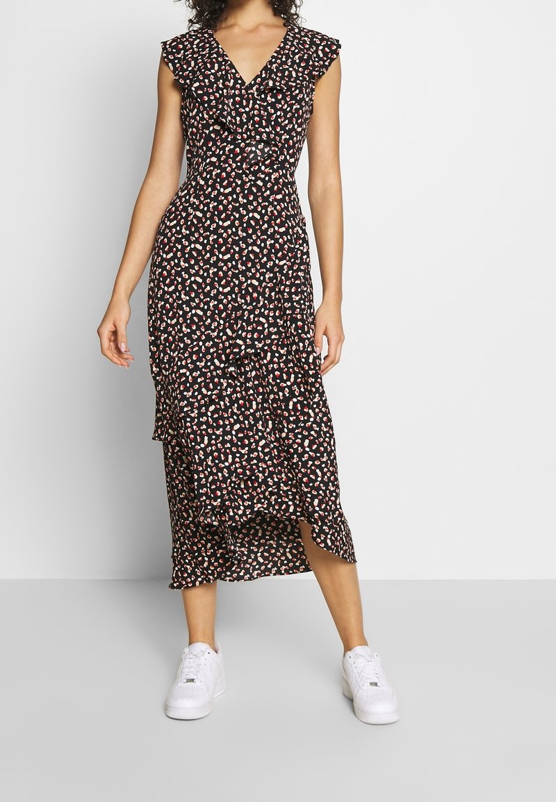 Vestido negro con estampado floral y mangas acampanadas con volantes, con un diseño en capas y longitud midi, combinado con zapatillas blancas.