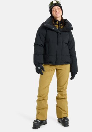 Svart boblejakke, khaki skibukser, svarte hansker og briller. Jakken har en firkantet form og har et quiltet tekstur.