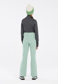 Haut à manches longues noir et blanc avec un motif, pantalon vert menthe et un bonnet en tricot vert et crème. Caractéristiques d'une coupe ajustée et de jambes de pantalon larges.