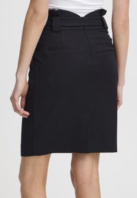 Jupe crayon noire avec une ceinture ornée d'un nœud, poches au dos et tissu lisse et texturé. Longueur mi-cuisse.