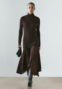 Bruine coltrui gecombineerd met een vloeiende bruine maxi-rok, voorzien van een gestructureerde stof en een enkel lengte, aangevuld met kniehoge laarzen.