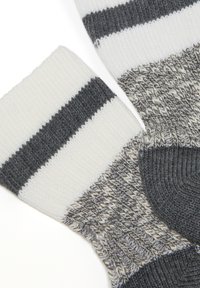 Gestrickte Socken in Weiß und Grau mit horizontalen Streifenmustern. Sie verfügen über ein strukturiertes Gewebe und kontrastierende Farbakzente am Bündchen und an der Zehe.