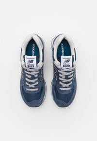 Blaue Wildleder- und Mesh-Sneaker mit einem grauen Schnürsystem, ausgestattet mit einem gepolsterten Kragen und einer Zunge, sowie New Balance-Branding auf der Zunge und der Seite.