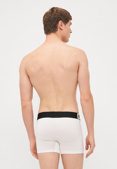 Weiße Boxershorts mit einem schwarzen Bund, aus glattem Stoff und eng anliegend, von hinten auf einem hellen Hintergrund zu sehen.