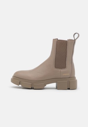 Bottine en cuir taupe avec semelle crantée épaisse, panneaux latéraux élastiques, languette de traction et petit logo doré "CPNHGN" près du talon.