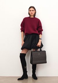 Bordeaux oversized sweater, sort nederdel, sort ruskindsstøvler til låret og en mønstret sort totebag med metalaccenter. Enkel og tekstureret design.