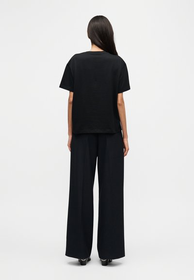Μαύρο βαμβακερό t-shirt με άνετη εφαρμογή, συνδυασμένο με μαύρο παντελόνι φαρδιάς γραμμής. Λείο ύφασμα, απλός σχεδιασμός, χωρίς ορατά μοτίβα ή διακοσμητικά στοιχεία.