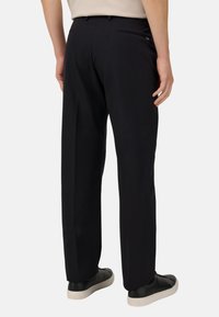 Černé kalhoty s rovně střiženými nohavicemi, hladkým materiálem a zadními kapsami, doplněné černými teniskami a béžovým topem.