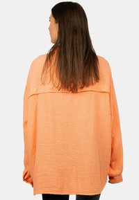 Camicia oversized a maniche lunghe in tessuto pesante color pesco con una spalla scesa e un'imbottitura sul retro.