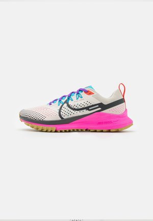 Lyse beige Nike trail løbesko med sort swoosh, lilla snørebånd, lys pink sål og rød hælkrog på hvid baggrund.