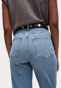 Hellblaue Denim-Jeans mit hoher Taille, fünf Taschen und einem schwarzen Gürtel mit silberner Hardware. Der Stoff hat eine klassische Textur.