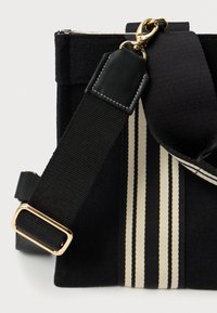 Borsa in tessuto nero con finitura testurizzata, dotata di una tracolla spessa a strisce beige e nere. Dettagli in metallo dorato e chiusura superiore con zip.