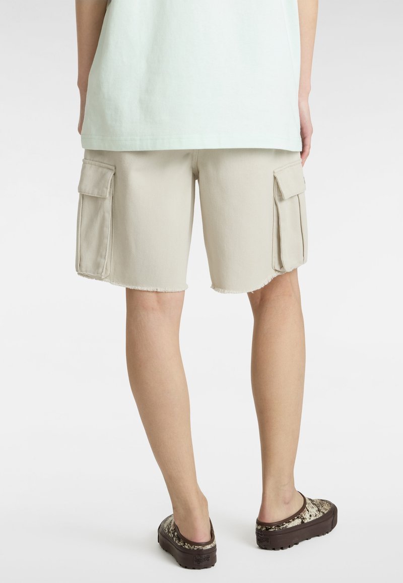 Bermudas beige con dobladillo deshilachado, que cuentan con dos grandes bolsillos laterales. Combinadas con una camiseta verde claro y zapatillas de lona estampadas.