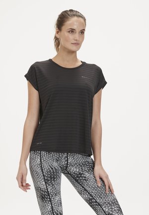 Schwarzes Sport-T-Shirt mit einem strukturierten Streifenmuster, kurzen Ärmeln und "Quick Dry"-Label; kombiniert mit geometrisch gemusterten Leggings in Schwarz und Weiß.