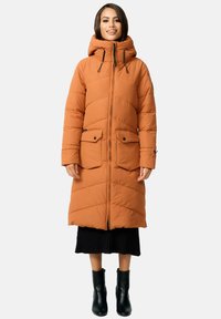 Long orange puffer coat with hood, featuring two front pockets, quilted design, and a zipper closure. Worn over a black ribbed skirt and boots.