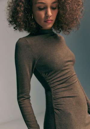 Abito lungo aderente marrone con maniche lunghe realizzato in un tessuto elastico, caratterizzato da un colletto alto e cuciture laterali arricciate, che creano una silhouette fluida.