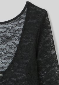 Top en dentelle noire avec un décolleté arrondi, des motifs floraux transparents et un tissu texturé. Les manches sont légèrement drapées, ce qui rehausse le design.
