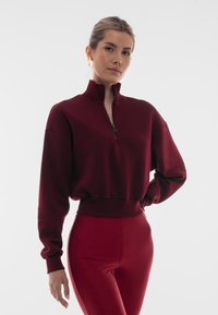 Burgundzki pół-zamek sweter z długimi rękawami, prążkowane mankiety i dół. W połączeniu z dopasowanymi legginsami o gładkiej fakturze.