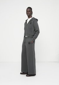 Γκρι cropped φούτερ με κορδόνια και λογότυπο λουλουδιού, σετ με φαρδιά παντελόνια φόρμας που φέρουν το ίδιο λογότυπο στο πλάι.