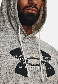 Grauer Kapuzenpullover mit schwarzem Under Armour-Logo und Text. Verfügt über Kordeln, ein strukturiertes Material und eine lockere Passform am Hals.