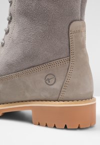 Stivaletto in suede grigio con suola in gomma, caratterizzato da una cucitura laterale e un dettaglio del logo sul lato. Lacci con accenti metallici.