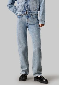 Jeans de mezclilla azul claro con un corte de pierna recta, costuras visibles, diseño de cinco bolsillos y textura desgastada, combinados con zapatos de plataforma negros brillantes.
