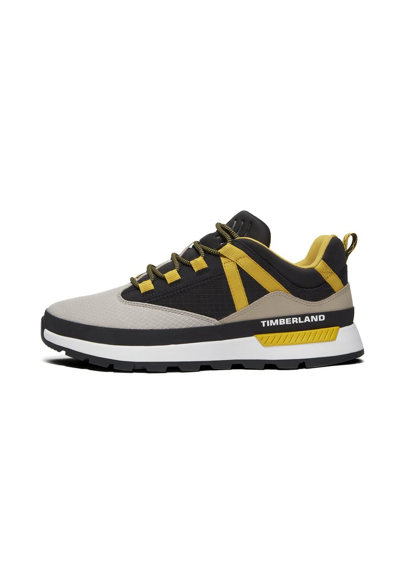Grijze en zwarte sneaker met gele accenten. Heeft een bovenwerk van mesh, een gevoerde zool en een karakteristieke "TIMBERLAND" branding aan de zijkant.