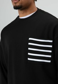 Zwarte sweatshirt van katoen, voorzien van een gestreept zakje in wit en zwart. Het ontwerp heeft een ronde hals en een textuurachtig stof.