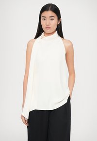 Balta bezroku blūze ar augstu apkakli un drapētiem sasienamajiem elementiem. Mīksts audums ar gludu tekstūru, kombinēts ar tumšām, platu staru biksēm.