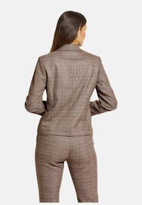 Brauner kariierter Blazer mit taillierter Passform. Das Material weist einen leicht strukturierten Stoff auf. Bemerkenswerte Details sind der Reverskragen und die schmale Silhouette.