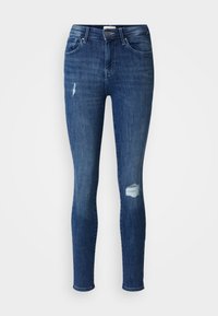 Vaqueros ajustados en denim azul oscuro con una textura suave. Presentan desgastes cerca de las rodillas y un clásico diseño de cinco bolsillos. Cierre de botón en la cintura.