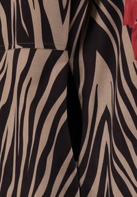 Zebramusterstoff in Beige und Schwarz mit glatter Textur; verfügt über einen runden Kragen und sichtbare Nähte entlang der Nähte.