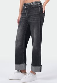 Zwarte denim wijde pijpen jeans met een rafelige zoom, eenvoudige zilveren hardware en zijzakken. G gedragen met witte sneakers.