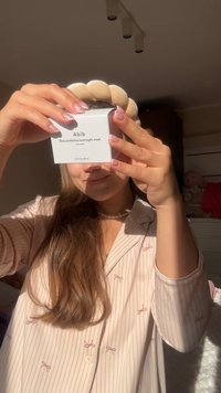 Abib Rice Probiotics Overnight Mask i en vit ask med svart text. Har en rund topp. Modellen bär en rosa randig skjorta.