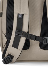 Beige hátizsák fekete párnázott hálós hátrésszel, állítható fekete nylon pántokkal, műanyag csatokka,l és egy kis textil címkével a válpánton.