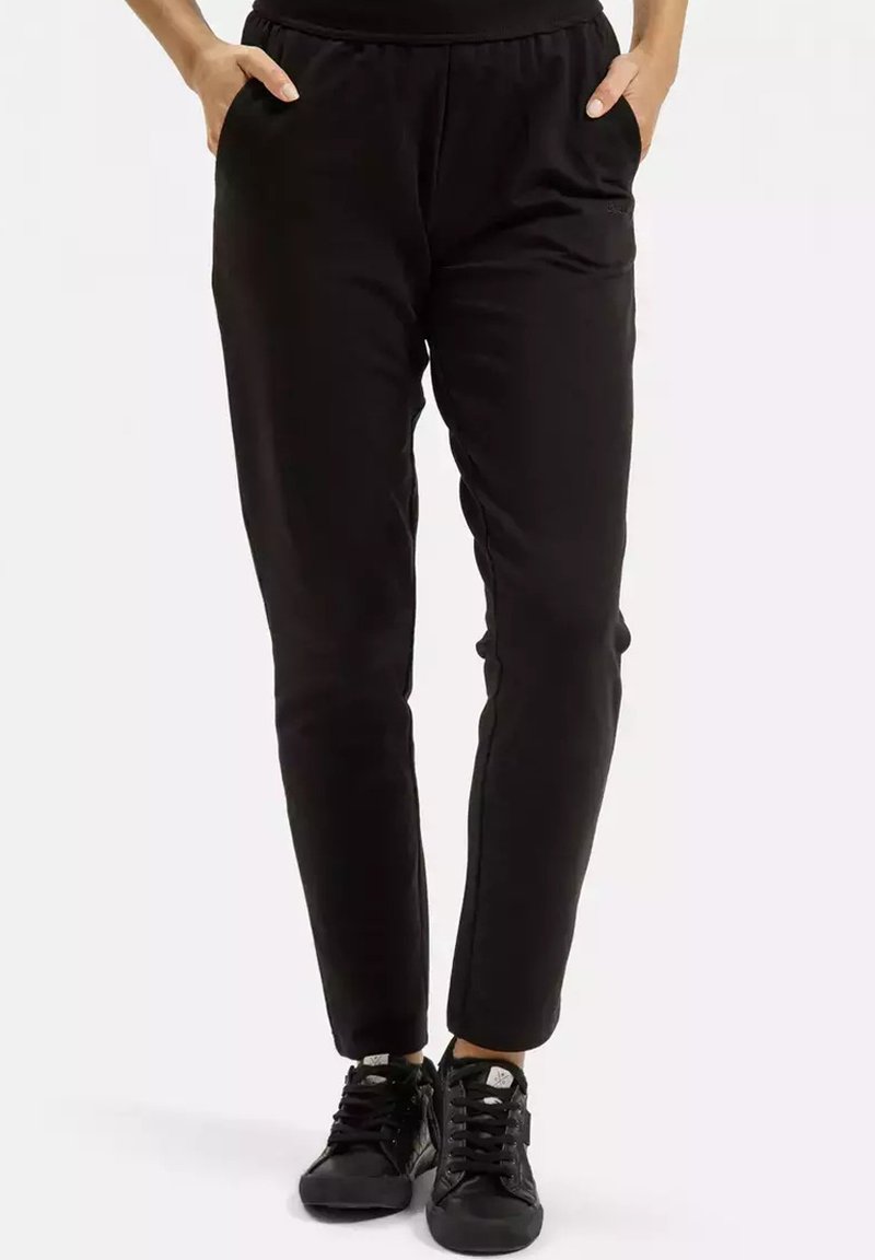 Czarne dresowe spodnie z elastycznym paskiem w talii, bocznymi kieszeniami, zwężanym krojem nogawek i miękką teksturą, w zestawie z czarnymi tenisówkami.