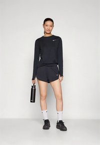 Musta urheiluvaate, jossa pitkähihaisen yläosan ja shortsit. Hän pitää kädessään mustaa vesipulloa, jalassa mustat lenkkarit ja valkoiset sukat. Nike-logo näkyvissä.